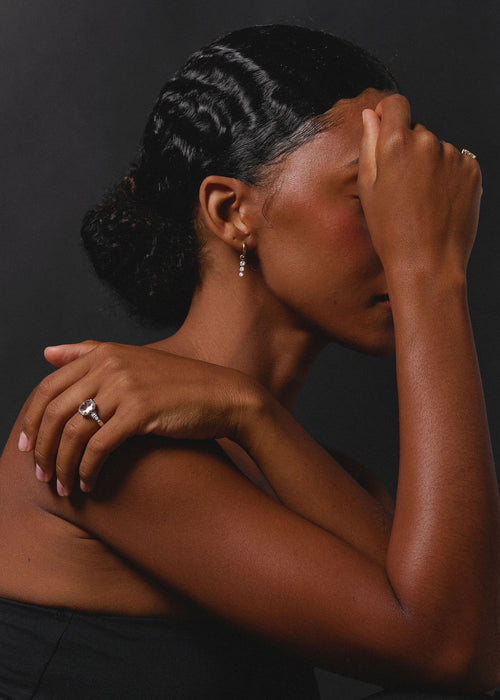 A woman in profile wearing a silver ring on her finger and a small drop earring, posed against a dark studio background. (view 5)