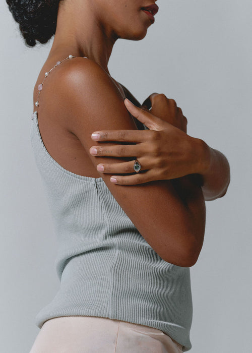 A shot of a model wearing a delicate silver chain shoulder bracelet adorned with small clear crystals, paired with a ribbed sage green tank top and light pink pants against a solid gray background. (view 5)