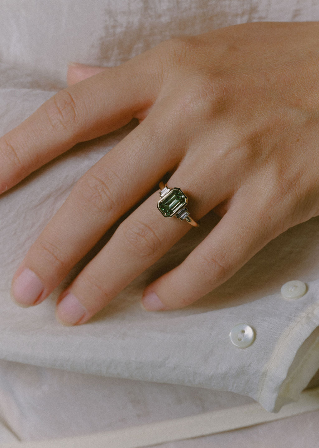 A yellow gold ring with a green diamond emerald center stone and white diamond side stones. (view 2)