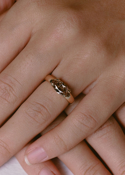 A close-up of a hand wearing a gold ring with an antique cut moval champagne diamond center stone. (view 6)