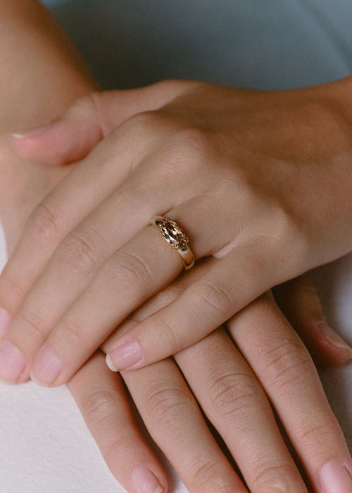 A close-up of a person's hands resting on a white surface, wearing a gold ring with a champagne gemstone. (view 2)