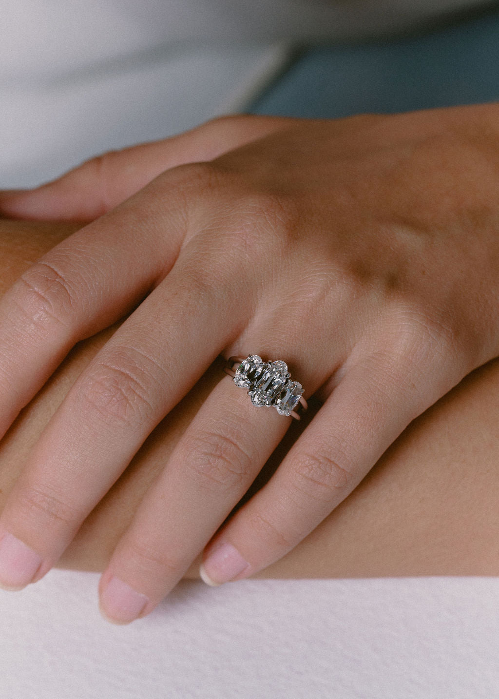 A close-up of a hand wearing a silver-toned ring with three round-cut clear gemstones, resting on a soft white surface. (view 7)