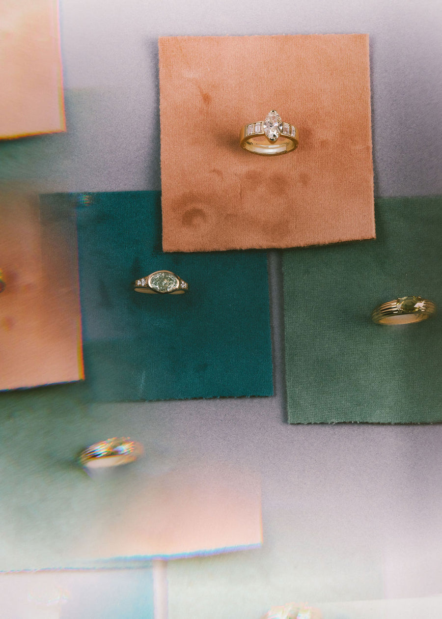 Gold rings with gemstones displayed on small square cards of different colors, including peach, teal, and sage green, against a soft lavender background.