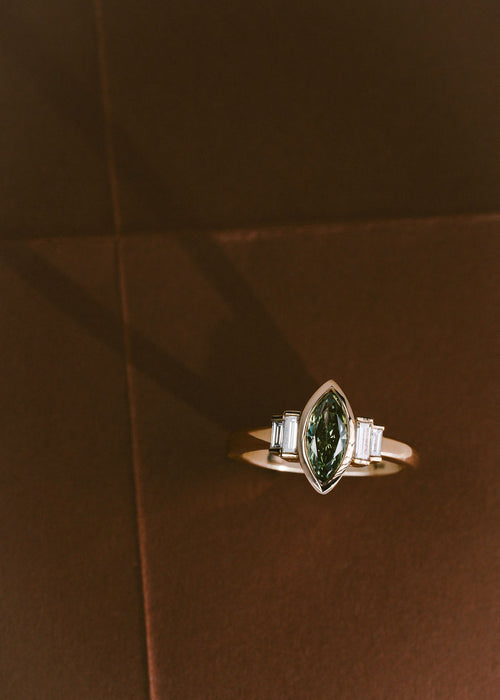 A yellow gold ring with a green diamond marquise center stone and white diamond side stones.