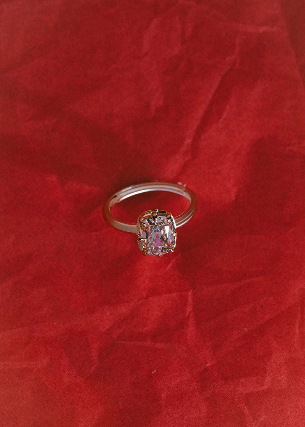 A gold ring with a rectangular champagne gemstone, displayed on a textured red fabric background. (view 5)