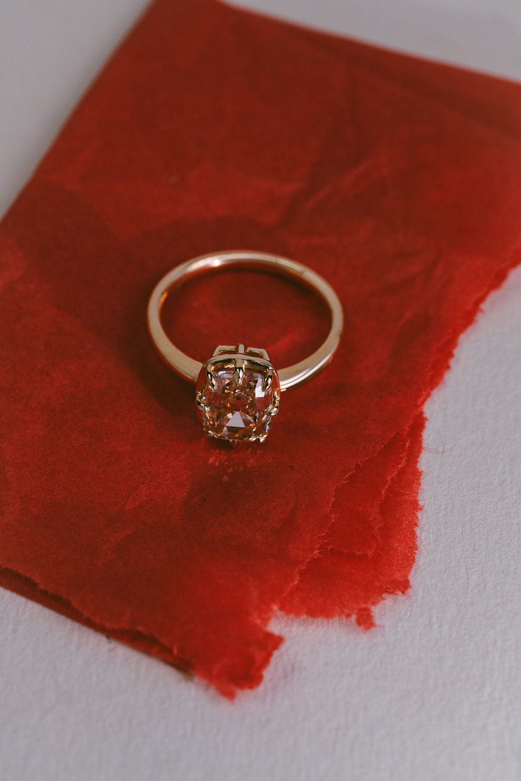 A gold ring with a large champagne cushion gemstone, resting on a textured red paper background. (view 10)