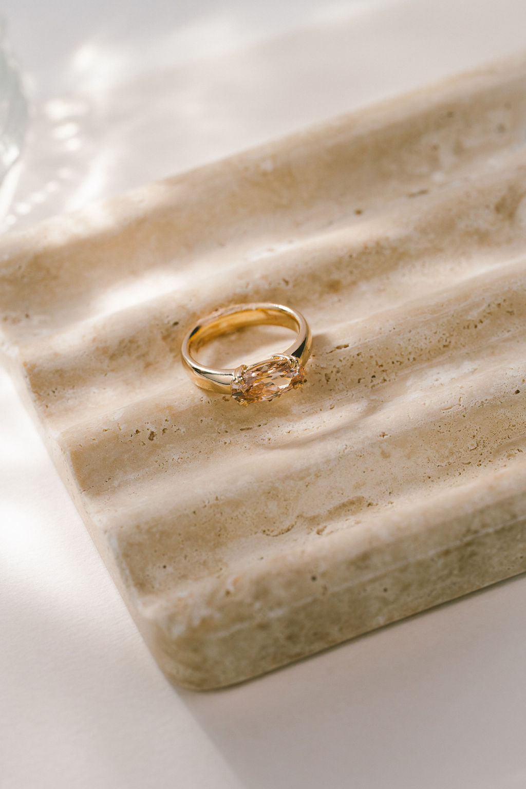 A gold ring with a champagne gemstone resting on a textured beige stone tray under soft, natural light. (view 9)