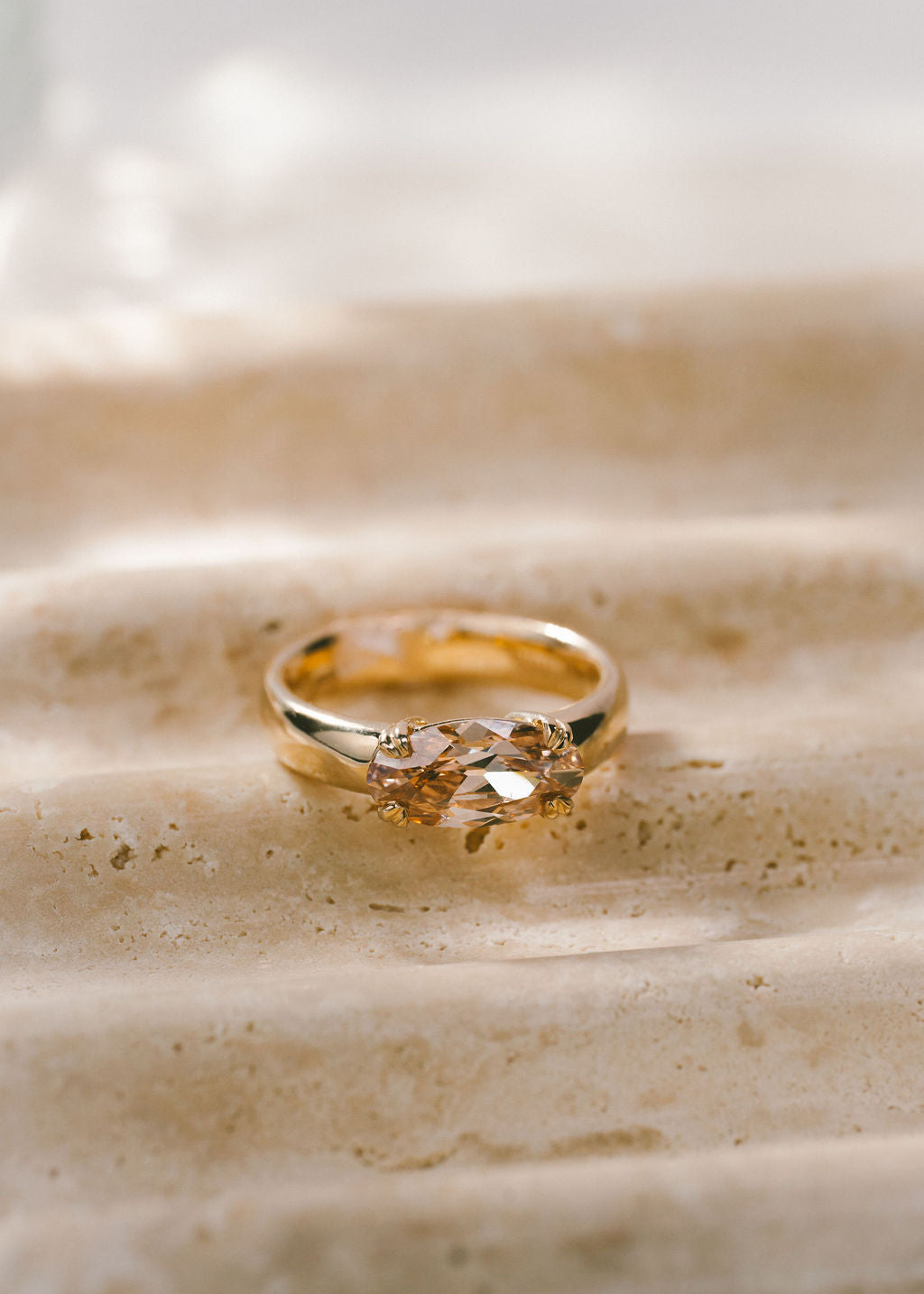 A gold ring with a moval cut champagne gemstone resting on a textured beige stone surface.