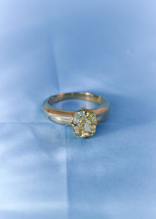 A  yellow gold solitaire ring with a yellow diamond, resting on a textured light blue surface.