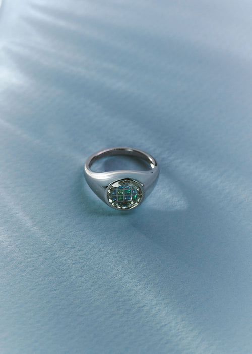 A silver signet ring with a round, textured green gemstone, resting on a textured light blue fabric background. (view 4)