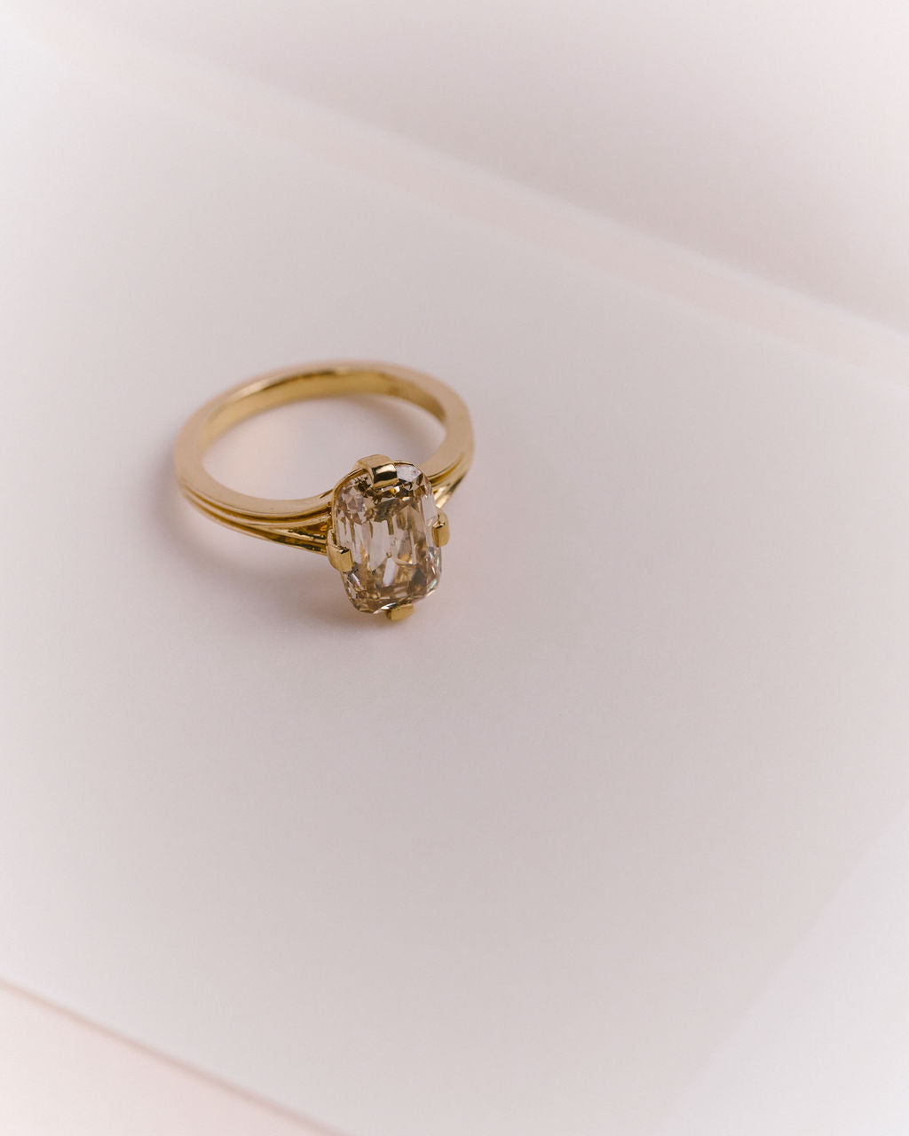 A gold ring with an champagne cushion cut diamond photographed on a clean, light-colored surface. (view 3)