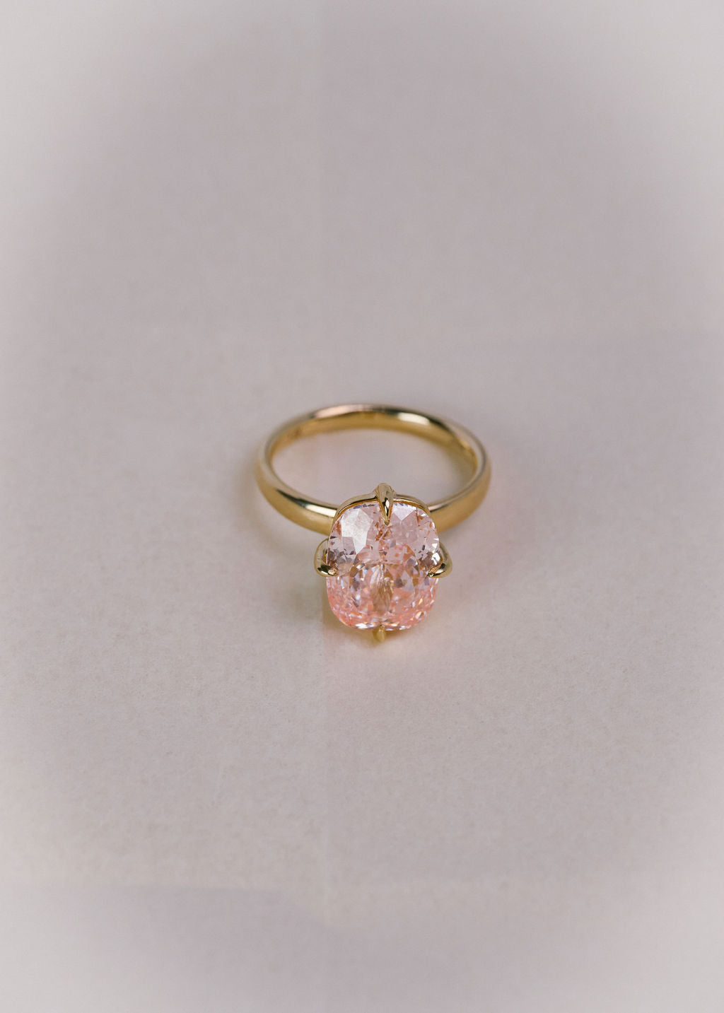 A gold ring with a large, pink cushion diamond, resting on a soft, textured white surface. (view 11)
